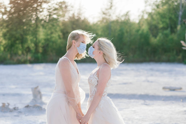 Lesbisch koppel bruiloft op wit zand, dragen maskers om epidemie te voorkomen COVID-19 - Foto, afbeelding