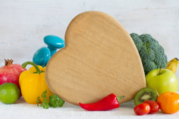 Kitchen board in the shape of heart, vegetables, fruits and dumbbells. Healthy diet and sport concept  - Foto, afbeelding