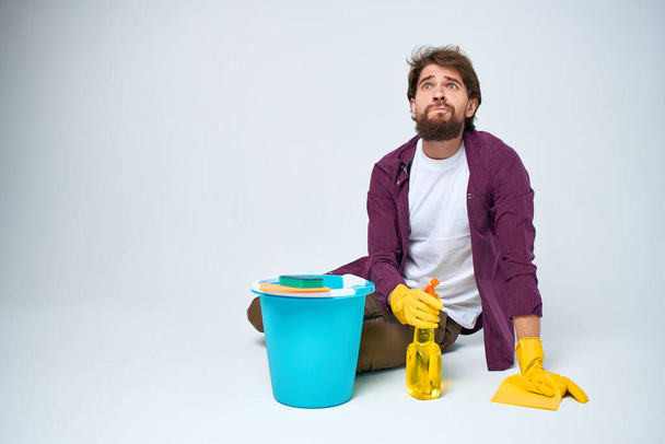 Un uomo si trova sul pavimento con un secchio di detergente servizio di pulizia sfondo leggero - Foto, immagini