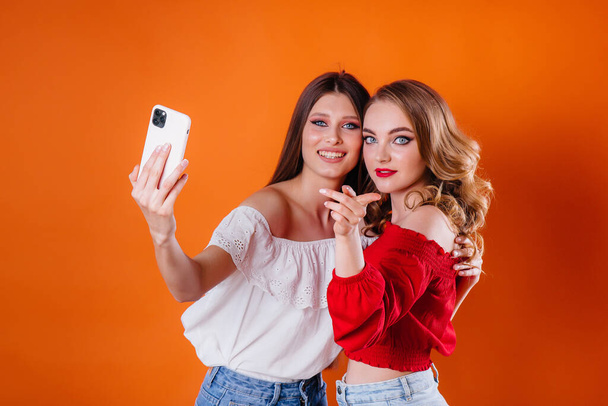 Dvě mladé a krásné dívky se selfie a sledovat telefon v ateliéru na fialovém pozadí. Dívky pro reklamu - Fotografie, Obrázek