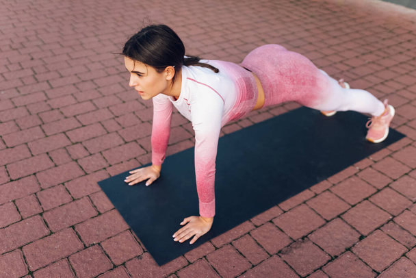 Slanke vrouwelijke atleet schudt de pers staande op plank - Foto, afbeelding