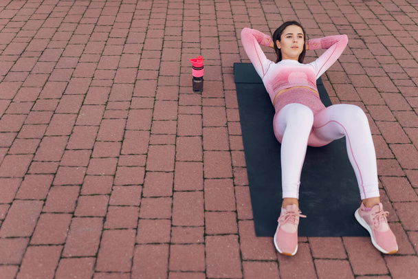 Schöne Fitness-Frau in pinkfarbener Sportbekleidung liegt auf Yogamatte und macht Bauch-Crunch-Übung  - Foto, Bild