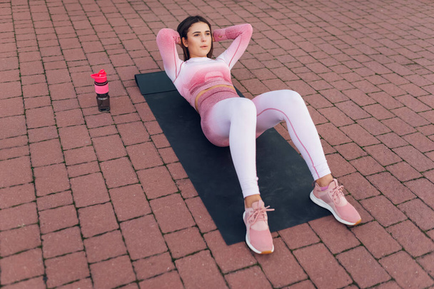 Piękna kobieta fitness w różowej odzieży sportowej leżącej na macie do jogi i wykonującej ćwiczenia brzuszne  - Zdjęcie, obraz