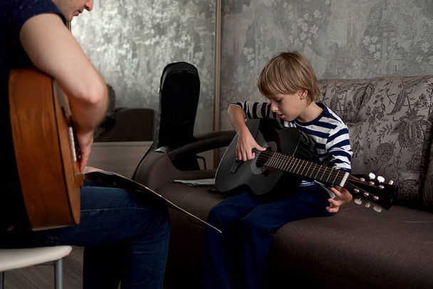 Young male musician teaches little boy student how to play the acoustic guitar and play by notes - Foto, immagini