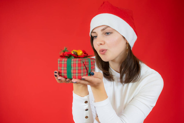 Portrait of an excited young woman wearing christmas hat isolated over red background holding surprise gift box. - Foto, Imagen