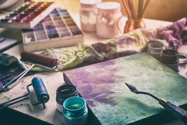芸術機器:キャンバスとパレットナイフ、ペイントブラシ、アーティストスタジオでの多色塗料. - 写真・画像