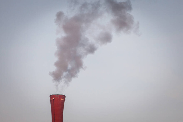 Industriële rode schoorsteen van een fabriek die giftige rookgassen en rookgassen in de atmosfeer afgeeft. - Foto, afbeelding