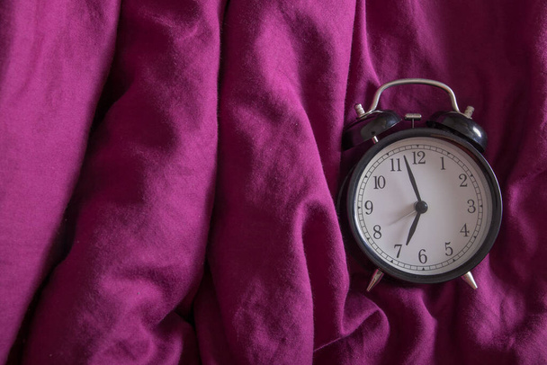Klassischer Wecker mit Morgenzeit auf einem Farbbett: Konzept des Morgenaufgangs - Foto, Bild