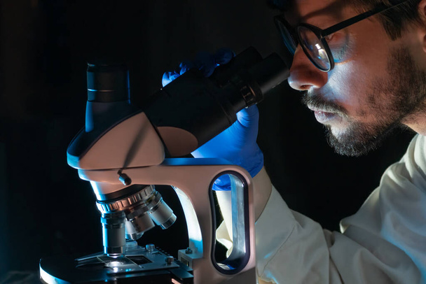 Científico está buscando en el microscopio en el laboratorio por la noche. Microbiología y concepto de investigación. - Foto, imagen