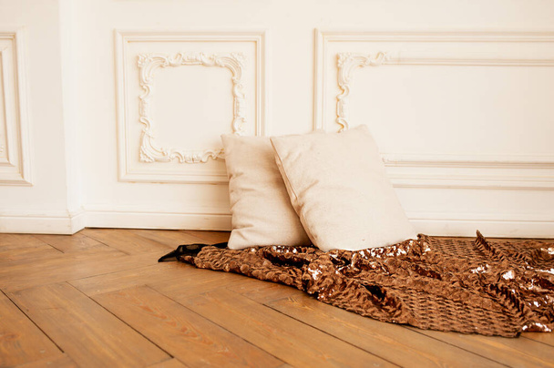 Zwei weiche, gemütliche beige Kissen auf dem Parkettboden mit einer glänzenden bronzefarbenen Decke und weißem Stuck an der Wand. Minimalismus im Innenraum, selektiver Fokus - Foto, Bild