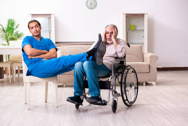 Vecchio in sedia a rotelle e giovane cattivo caregiver al chiuso - Foto, immagini