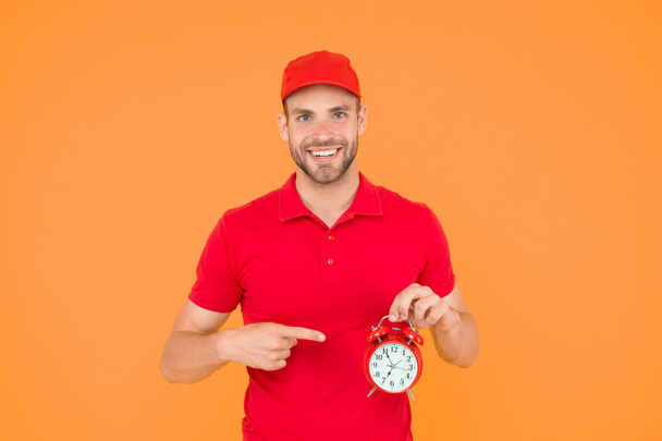 Always in time. Happy man with alarm clock on yellow background. Delivering your purchase. Courier service delivery. Salesman and courier career. Courier and delivery service. Postman delivery worker - Valokuva, kuva