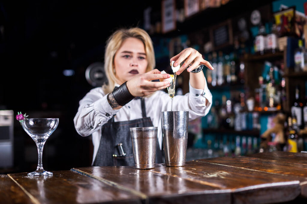 Pretty Girl Bartending macht einen Cocktail, während sie in der Nähe der Theke in einem Nachtclub steht - Foto, Bild