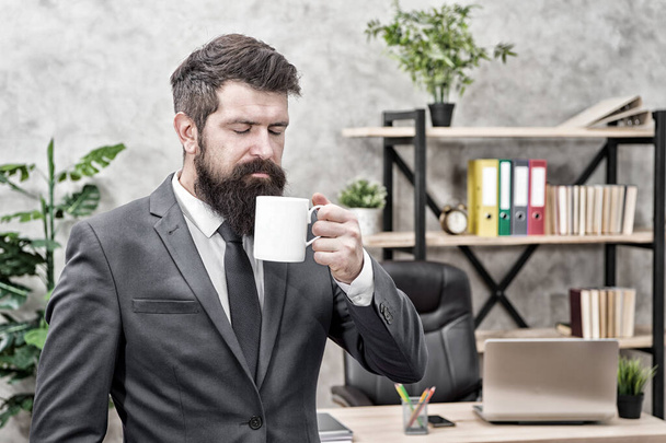 Drinking coffee relaxing break. Boss enjoying energy drink. Start day with coffee. Successful people drink coffee. Caffeine addicted. Man bearded businessman hold coffee cup stand office background - Fotoğraf, Görsel