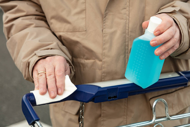 Mans Hand sostiene una botella de plástico con desinfectantes, para usar el mango de un carrito de compras desinfectarse - Foto, imagen