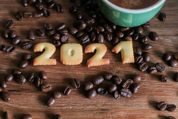 2021 kenyérszám és kávéscsésze fa asztalra kávébab.Boldog új évet 2021, Ünnepek élelmiszer művészet koncepció. (közelről) - Fotó, kép