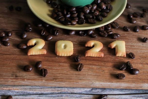 2021 leipänumero ja kahvikuppi puupöydällä kahvipapujen kanssa.Hyvää uutta vuotta 2021, Holidays food art concept. (lähikuva)) - Valokuva, kuva