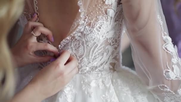 Bruidsmeisje bindt en helpt bij het aantrekken van trouwjurk. Ochtendbereiding van de bruid met witte jurk - Video