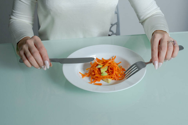 Meisje eet heerlijke wortelsalade in de keuken.  - Foto, afbeelding