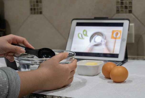 Hausfrau lernt, wie man Pfannkuchen zubereitet, indem man zu Hause ein Online-Video anschaut - Foto, Bild