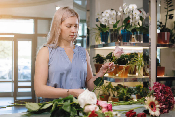 Blonde florist fums a bouquet in the working space of a flower shop. Selective focus. - Φωτογραφία, εικόνα