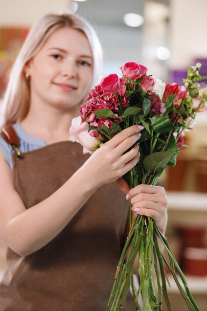 Blond florist woman in apron in workspace of flower shop. Selective focus. - Photo, image