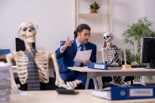 Jovem funcionário do sexo masculino com esqueletos no escritório - Foto, Imagem
