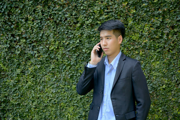 Fiatal ázsiai üzletember sétál a parkban egy okostelefonnal. - Fotó, kép