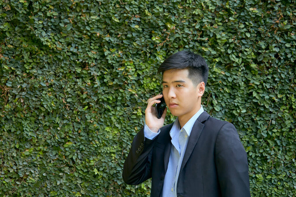 Mladý asijský podnikatel procházky v parku pomocí chytrého telefonu. - Fotografie, Obrázek