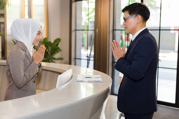 Ένας μουσουλμάνος ρεσεψιονίστ εισάγει ένα ευγενικό χαιρετισμό στους επισκέπτες του ξενοδοχείου. - Φωτογραφία, εικόνα