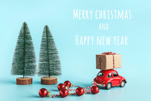 Small red car carries gift box and christmas tree with copy space. Concept Happy new year and Merry christmas. Template for design, postcard, invitation. Novosibirsk, Russia - October 20, 2019. - 写真・画像