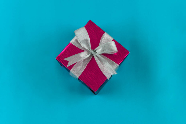 Vue du dessus de la boîte cadeau enveloppée dans du papier rouge avec ruban sur fond bleu. Espace de copie pour le texte. Concept de vacances. Cadeaux de temps. - Photo, image