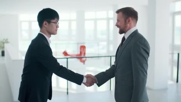 Vista lateral metraje plano medio de dos hombres de negocios adultos jóvenes saludándose con apretón de manos y hablando de algo - Metraje, vídeo