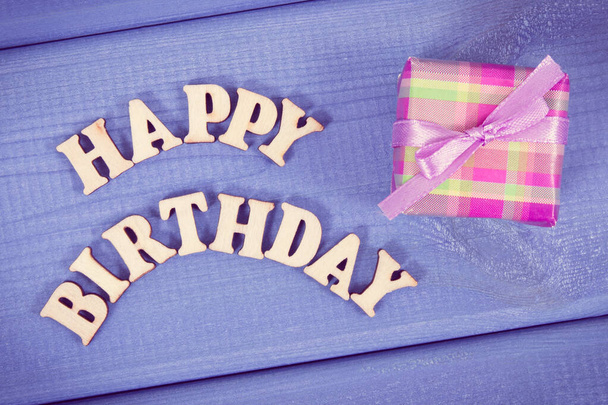 Wrapped gift with ribbon for birthday. Inscription happy birthday on purple boards - Foto, Bild