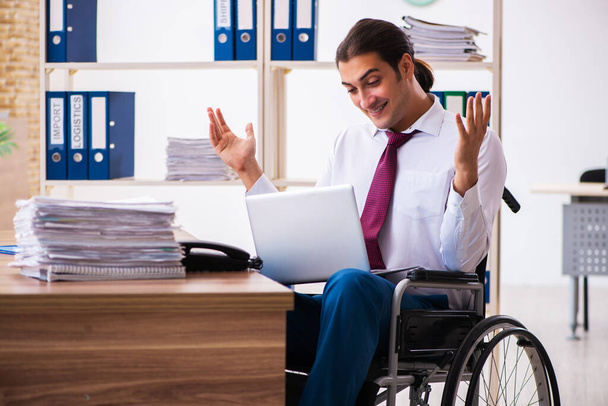 Νεαρός άνδρας εργαζόμενος μετά από ατύχημα σε αναπηρική καρέκλα στο χώρο εργασίας - Φωτογραφία, εικόνα