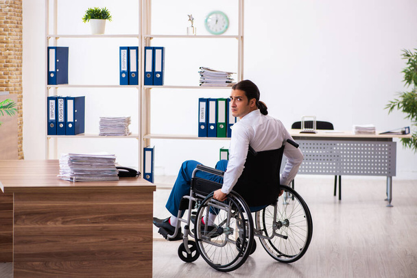 Νεαρός άνδρας εργαζόμενος μετά από ατύχημα σε αναπηρική καρέκλα στο χώρο εργασίας - Φωτογραφία, εικόνα