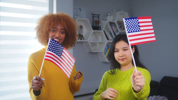 Amistad e igualdad multirraciales. Mujer afroamericana y asiática sosteniendo banderas de Estados Unidos. Programa de intercambio de estudiantes - Foto, imagen