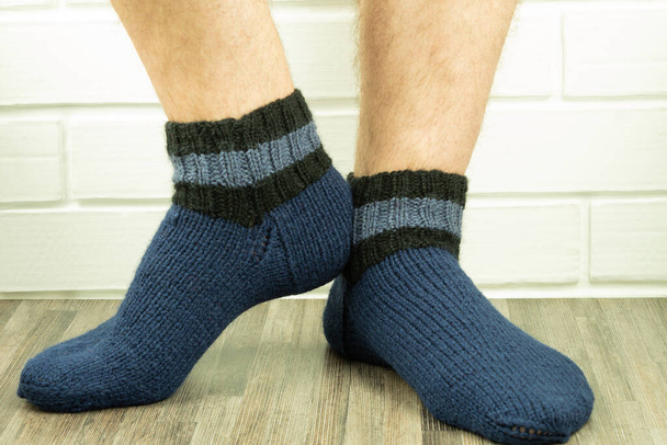 Handgemachte Socken, warme und selbst gestrickte Socken in Nahaufnahme. Foto von Männerbeinen in Stricksocken in Nahaufnahme. Geschäftsidee, Geld verdienen für ein Hobby. Nützliche Fähigkeiten unter Quarantäne - Foto, Bild
