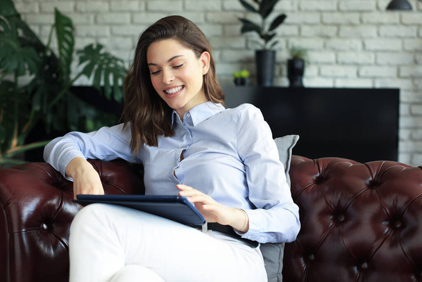 Young smiling woman with tablet pc on the sofa - Foto, afbeelding