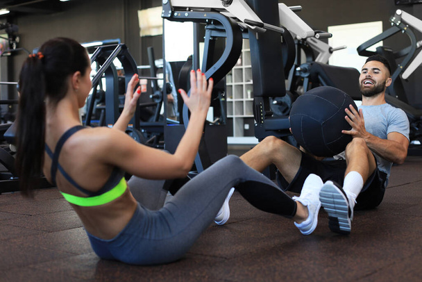Beautiful young sports couple is working out with medicine ball in gym - Foto, imagen