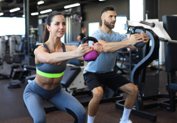 Fit and muscular couple focused on lifting a dumbbell during an exercise class in a gym - Фото, изображение