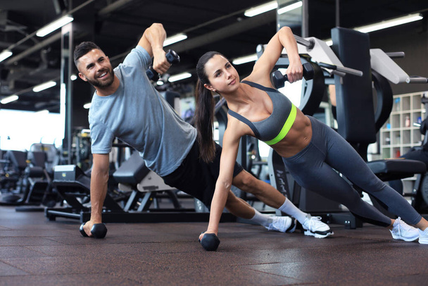 Strong man and woman holding dumbbells in plank position at the gym - Fotó, kép