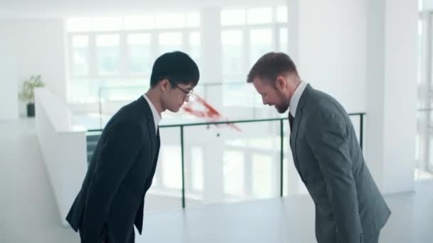Vista lateral filmagem de tiro médio do homem caucasiano moderno cumprimentando seu colega asiático com arco e começando a falar sobre negócios - Filmagem, Vídeo