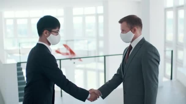 Zwei unkenntlich gemachte männliche Büroangestellte mit Schutzmasken begrüßen sich mit Handschlag, Seitenansicht - Filmmaterial, Video