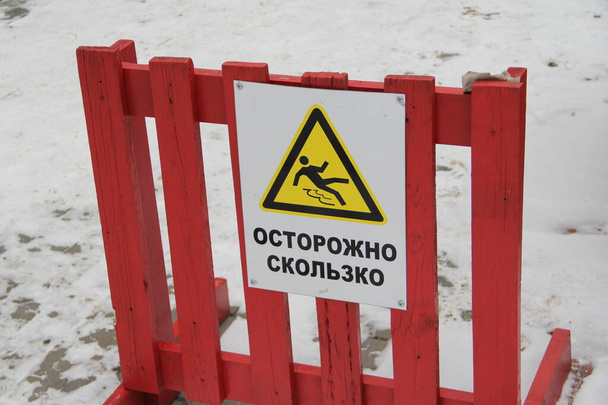 Syktyvkar, Russia -11.13.2020. Caution slippery sign on a wooden red fence. Black silhouette of a falling man against the background of a yellow triangle with black outline - Foto, imagen