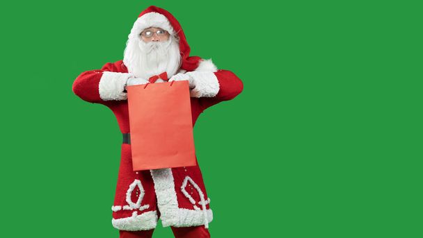 Święty Mikołaj na zielonym tle z czerwoną torbą na zakupy. Przestrzeń kopiowania. - Zdjęcie, obraz