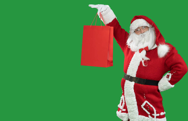 Yeşil arka plandaki Noel Baba 'nın elinde kırmızı bir alışveriş torbası var. Boşluğu kopyala. - Fotoğraf, Görsel
