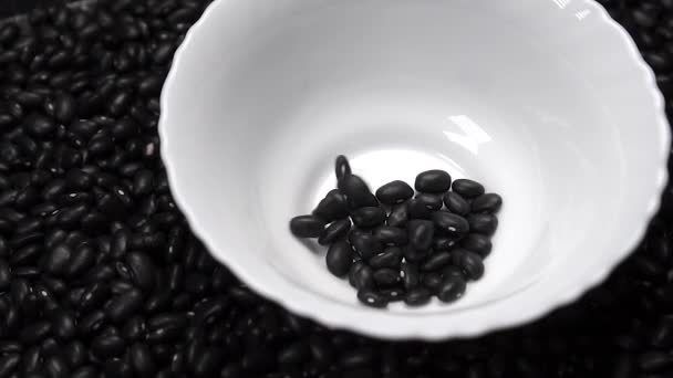 Black beans fall into a white ceramic bowl in a pile of legumes. Slow motion. Rotation - 映像、動画