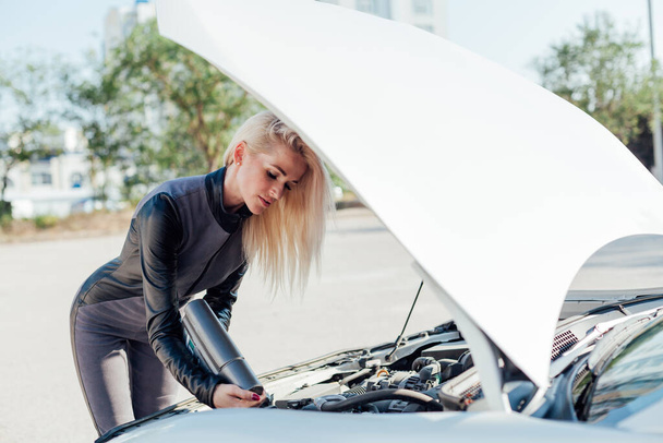 Beautiful female blonde driver repairs motor under car hood - Foto, Imagen