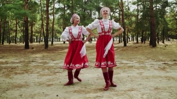 Две молодые и красивые женщины танцуют русские традиционные танцы в летнем лесу - Кадры, видео